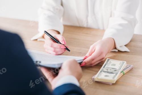 Preview: cropped shot of woman signing contract on clipboard in hands of manager near dollar banknotes on