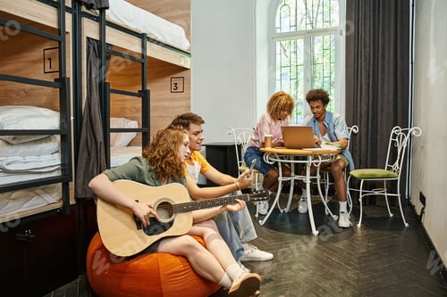 Preview: multicultural students with guitar and laptop in room of contemporary youth hostel, travelers