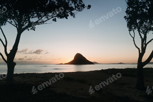 Preview: Silhouette shot of a small island in the ocean with a clear blue sky in the background