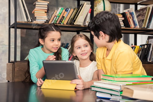 Preview: Children using digital tablet and looking at each other in library