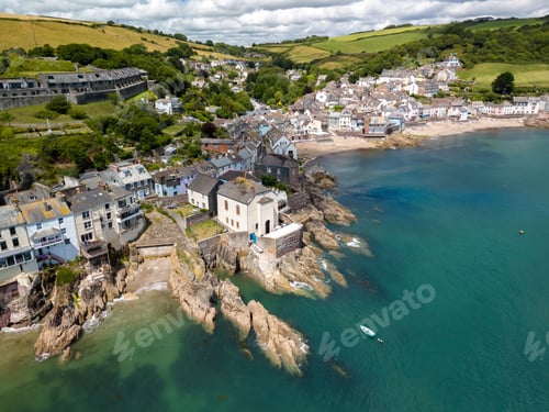 Preview: a coastal village with houses on cliffs and a beach, surrounded by green hills and a blue sea.