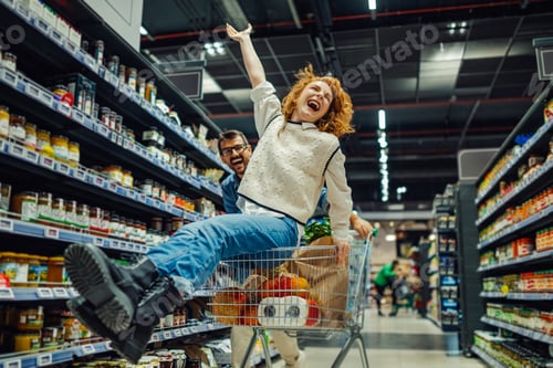 Preview: Cheerful couple having fun riding shopping cart in supermarket