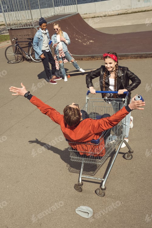 Preview: teenagers having fun with shopping cart in skateboard park, hipster style concept
