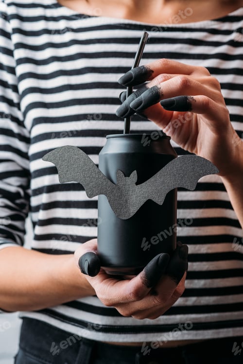 Preview: cropped shot of woman holding black can of soda with bat sticker, halloween concept