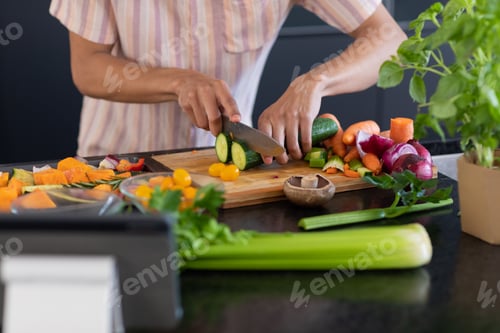 Preview: Midsection of biracial man cooking, chopping vegetables in kitchen