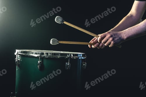 Preview: A man plays a musical percussion instrument with sticks on a dark background.