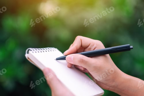 Preview: Closeup image of a woman holding and writing on blank notebook in the outdoors