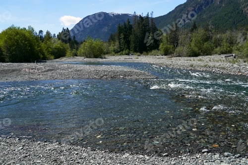 Preview: A gravel river bed leading to the distant dense forest and mountains.