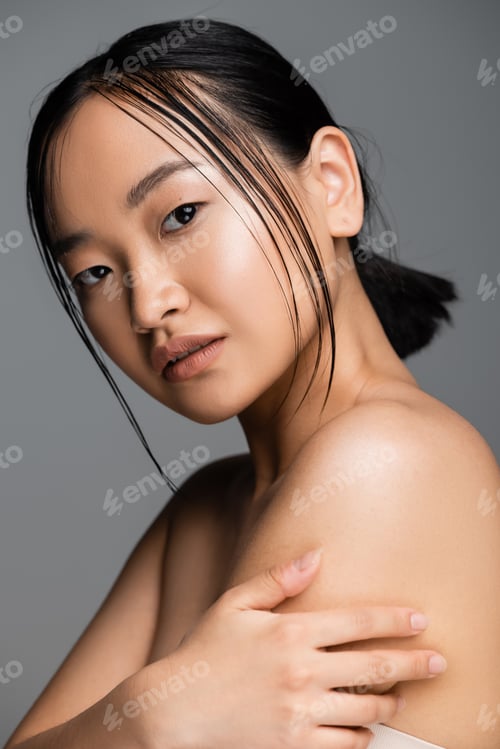 Preview: portrait of brunette asian woman with natural makeup touching bare shoulder and looking at camera