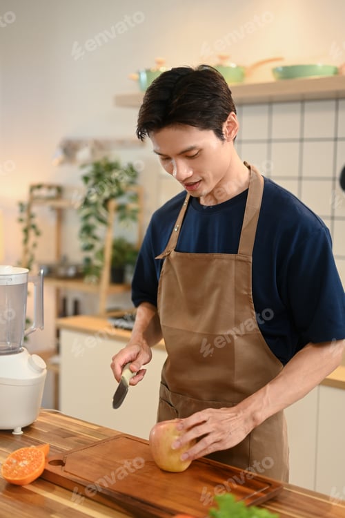 Preview: Handsome adult man wearing apron making healthy smoothie on kitchen counter