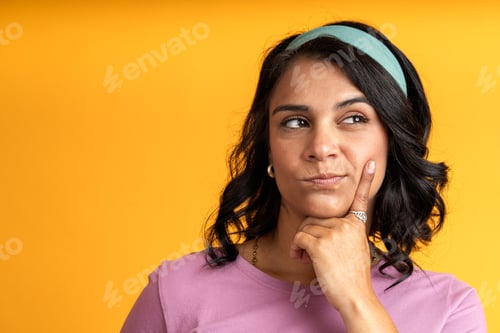 Preview: Pensive young woman making a decision on vibrant yellow background