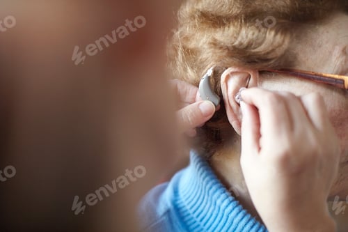 Preview: Mature woman helping senior woman insert hearing aid, close-up, differential focus