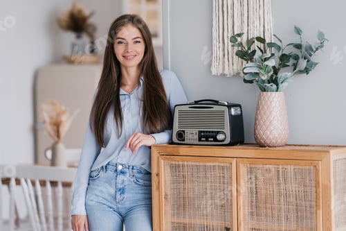 Preview: Gorgeous caucasian woman with loose long hair dressed in blue shirt and jeans stands at living room