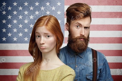 Vista previa: Young couple standing against US flag background: pretty woman pouting with sad and disappointed exp