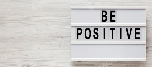 Preview: 'Be positive' words on a lightbox on a white wooden background, top view.