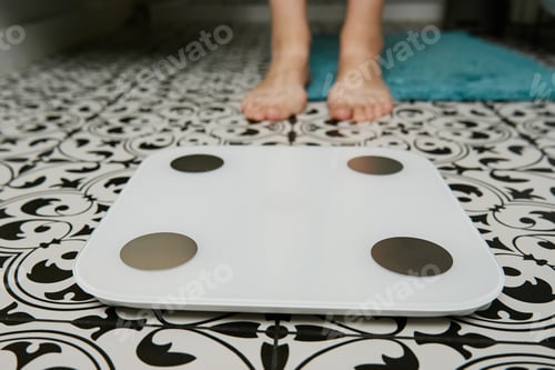 Preview: Woman checking her weight on weighing scales in bathroom