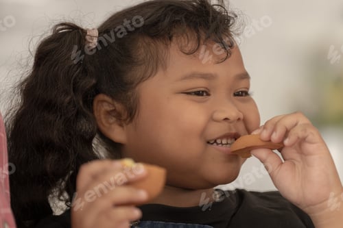 Preview: close up face of a Cute Asian girl eating a snack with family