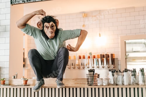 Preview: Man wearing monkey mask, sitting on counter of a bar, scratching head