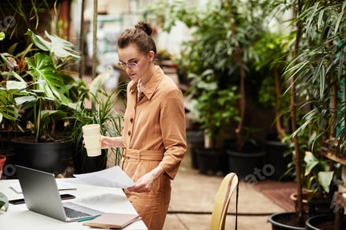 Preview: Young serious businesswoman with drink working with documentation