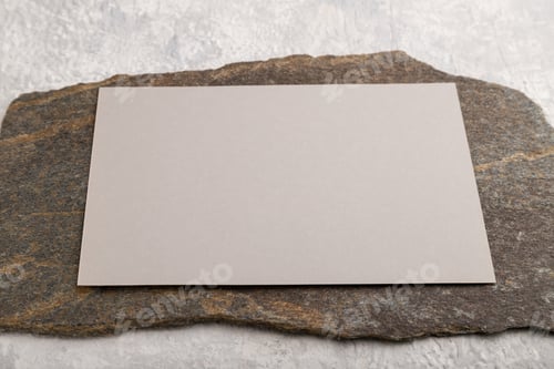 Preview: Beige paper business card, mockup with stone on gray concrete background. side view, copy space.