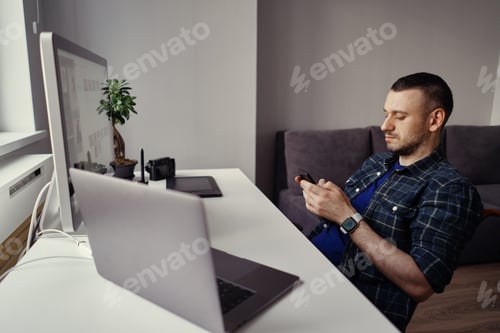 Preview: Young man holding smartphone in hands while making a pause in home office