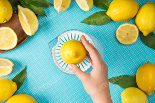 Preview: top view of female hand with lemons and squeezer on turquoise background