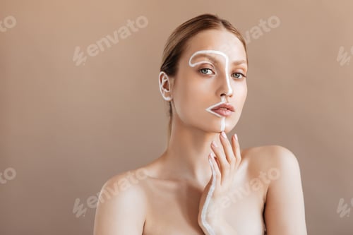 Preview: Young woman without makeup with clean skin looks into camera on beige background. Portrait of girl