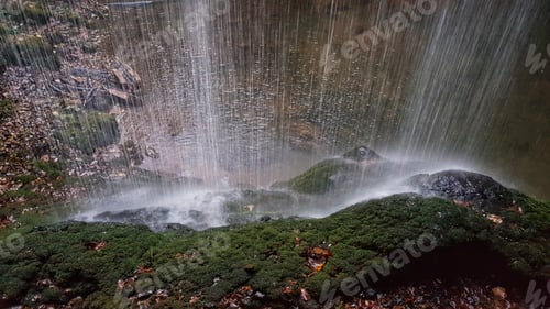 Preview: Water from a waterfall falling and splashing on a green mossy rock.