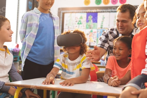 Preview: Front view of a schoolboy using virtual reality headset with his classmate and teacher at school
