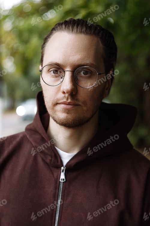 Preview: Young man in brown hoodie standing on park path