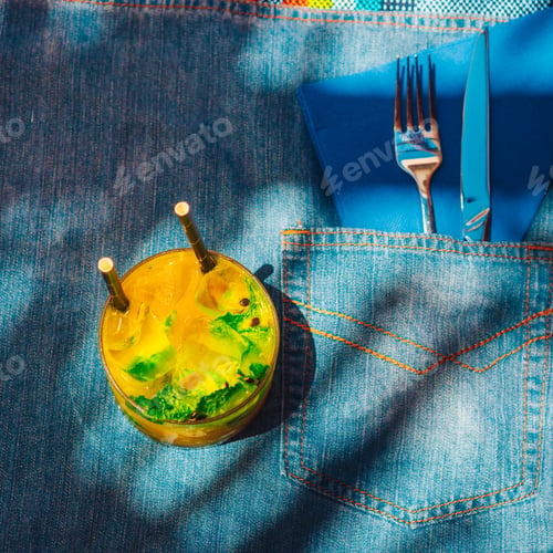Preview: Top view of a cocktail on a denim table placemat with knife and fork in the pocket