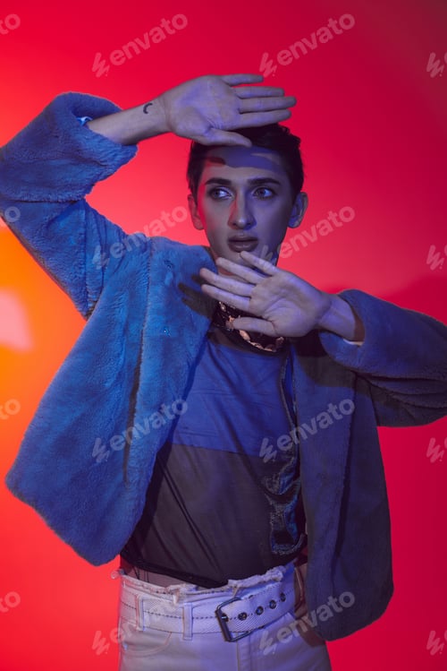 Preview: attractive modish androgynous man in purple faux fur posing on vibrant backdrop and looking away