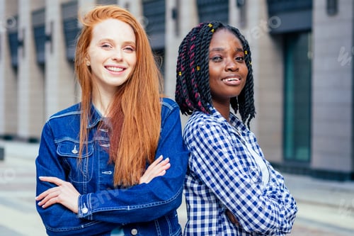 Preview: cheerful afro and european lesbian women laughing and looking at camera at summer downtown city