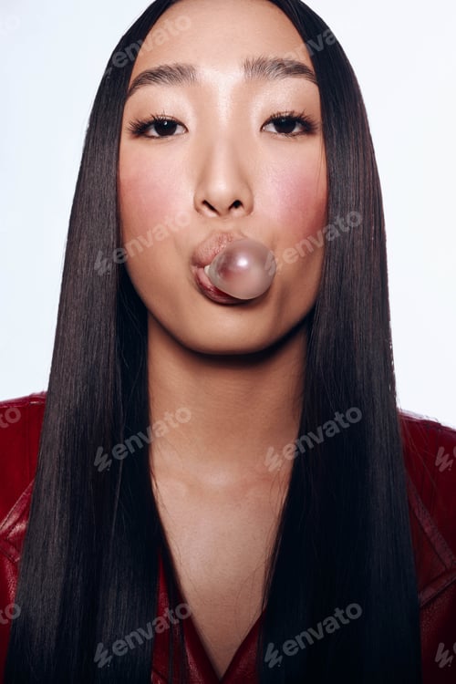 Preview: Asian woman with long black hair blowing a bubble against a white background