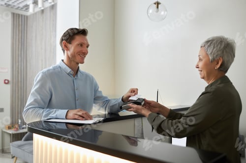 Preview: Smiling elegant man paying in medical clinic via NFC technology