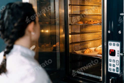 Preview: attractive baker takes ready buns and croissants from professional oven bakery production