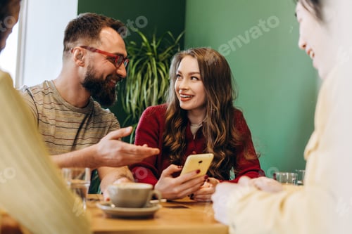 Preview: Friends enjoying time together, talking and using phone in cafe