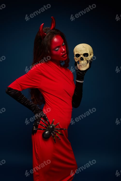Preview: A stunning woman in a red Halloween costume poses with a skull and spider against a dark backdrop