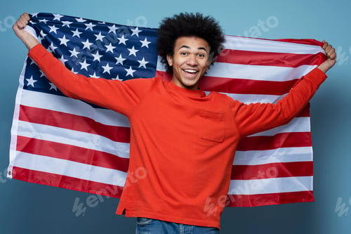 Preview: Portrait of happy confident African American man holding American flag isolated on blue background