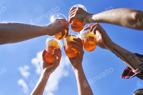 Preview: Low angle view of hands toasting beer on blue sky at festival