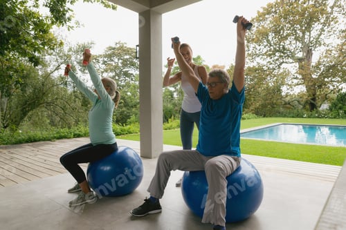 Preview: Caucasian female trainer assisting active senior couple to exercise with dumbbell in the porch