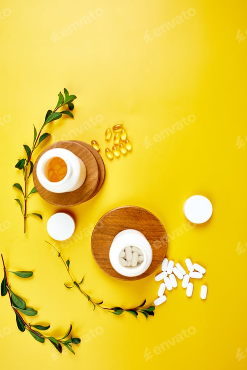 Preview: Flat lay of pills, fish oil, vitamins with green leavws on yellow background