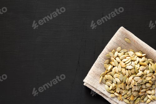 Preview: Roasted pumpkin seeds on cloth over black background, top view. Flat lay, overhead, from above.