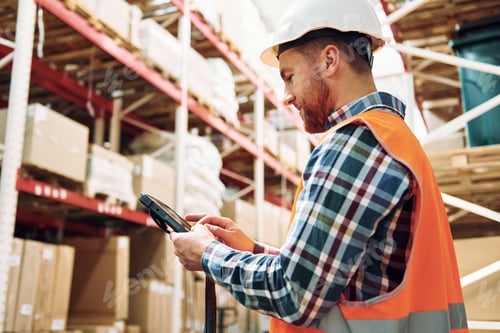 Preview: Holding tablet in hands. Employee in uniform is working in the storage at daytime