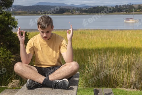 Preview: Teenage boy having a mindful meditation moment beside the river