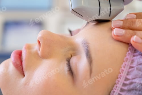 Preview: Cosmetologist making a woman a therapeutic laser processing on a face.