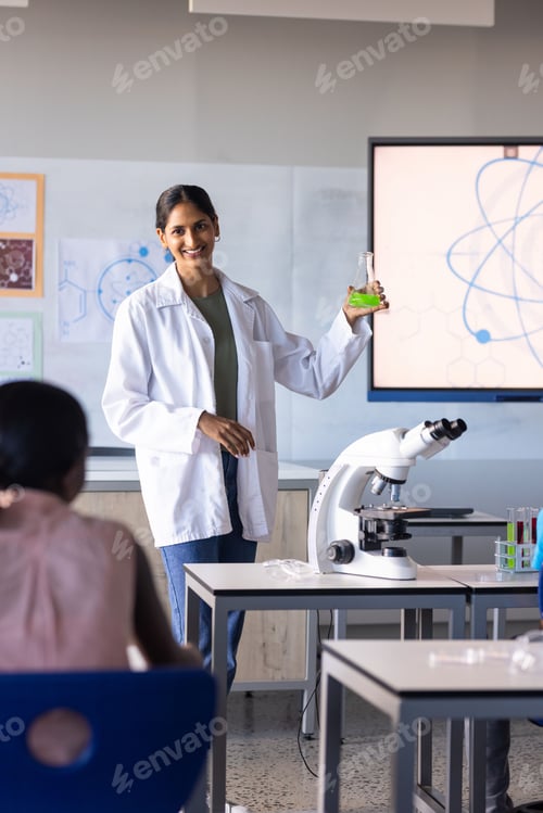 Preview: In school, Indian female teacher holding flask and explaining science experiment to students