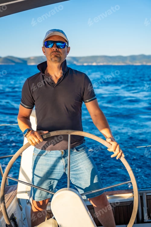 Preview: Young man captain stands at the helm and controls a sailboat during a journey by sea