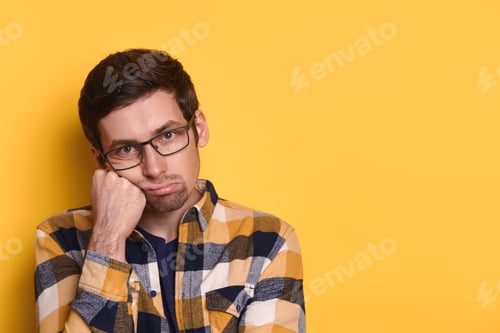 Preview: Closeup bored tired guy posing against yellow studio wall with copy space