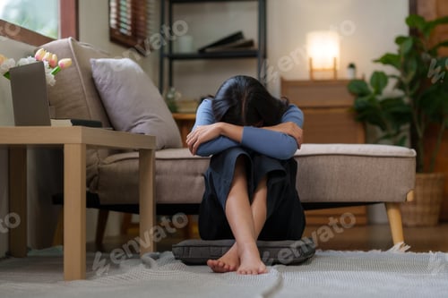 Preview: Young Asian woman suffering from stress sit alone at home, dejected.